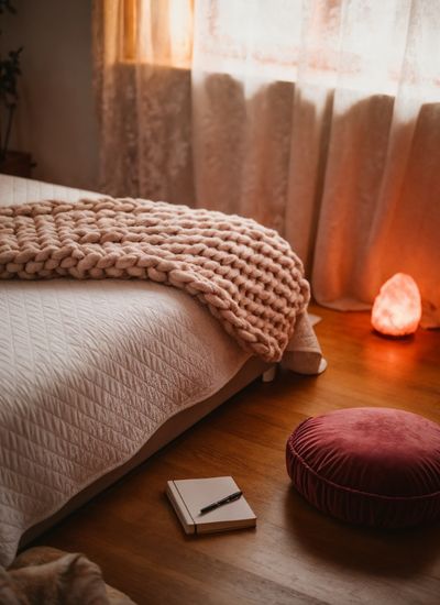 A calm relaxing space with journal and salt lamp on the floor beside a bed and sitting pillow